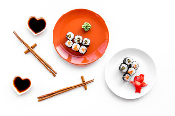 Sushi roll with salmon and avocado on plate with soy sauce, chopstick, wasabi on white background top view