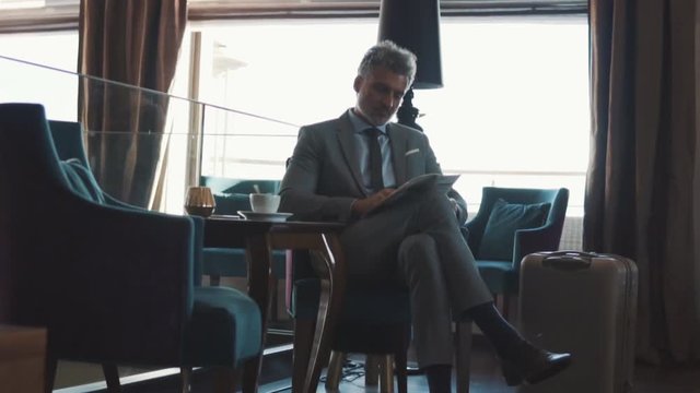 Mature businessman reading newspapers in a hotel lobby.