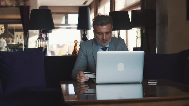 Mature businessman with laptop in a hotel lounge.