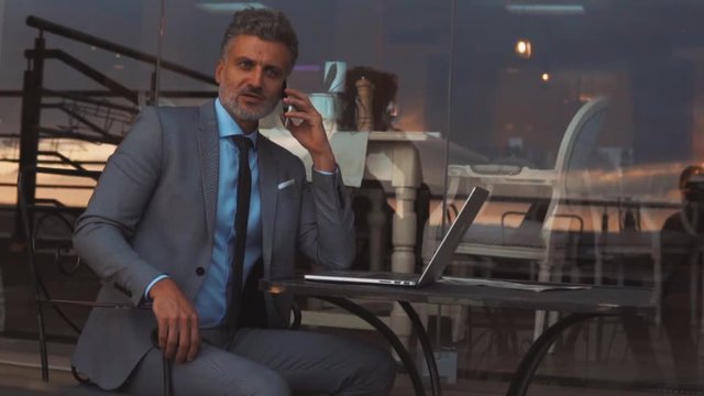 Mature businessman with smartphone outside a cafe.