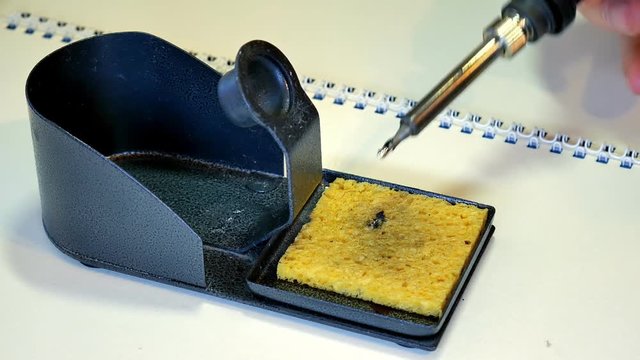 Cleaning the hot tip of his soldering iron on a wet sponge pad.
