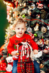 Funny little boy plays before a rich Christmas tree