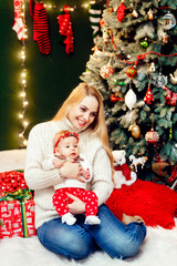 Blonde woman in white sweater sits with little girl before a Christmas tree