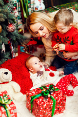 Fototapeta na wymiar Blonde mom plays with her son and daughter before a Christmas tree