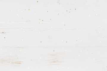 Small golden stars confetti on white wooden background.
