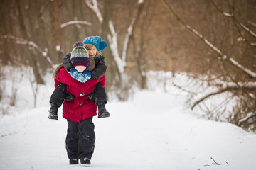 Fototapeta na wymiar Cute kid boy carrying his friend while walking in a winter park..Children playing and having fun.