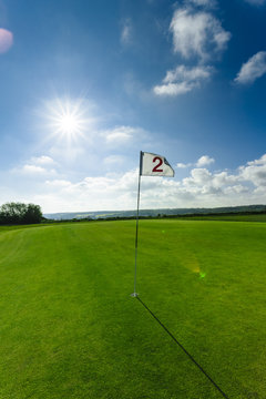 View of a green golf course, hole and flag on a bright sunny day. Sport, relax, recreation and leisure concept. Summer landscape with sunbeams