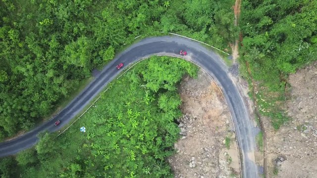 Drone flies over the curve road near the green mountain on which drivers driving a sports atv