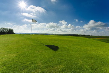 View of a green golf course, hole and flag on a bright sunny day. Sport, relax, recreation and leisure concept. Summer landscape with sunbeams