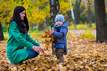 Mother with little son play and smiles in park on background of colorful autumn fallen leaves