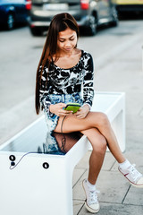 Beautiful woman charging her phone on free multipurpose solar panel charger incorporated in to sitting bench for citizens.Modern technology free energy for everyone . © Ivan Trizlic