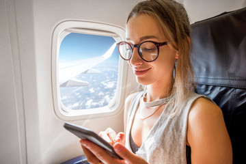 Obraz premium Young woman sitting with phone on the aircraft seat near the window during the flight in the airplane