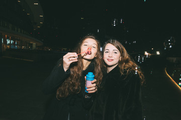 two young women outdoor night life playing bubble soap - happiness, getting away from it all, childhood concept