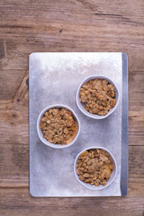 Ceramic ramekins with apple crumble  on a baking tray. Wooden background. Copy space. 