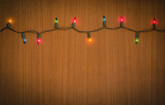 Christmas light bulbs turned on or lid on string in multi colours; blue, yellow, red, pink, orange and green on dark teakwood background at night time, Xmas or new year holiday decoration ornament