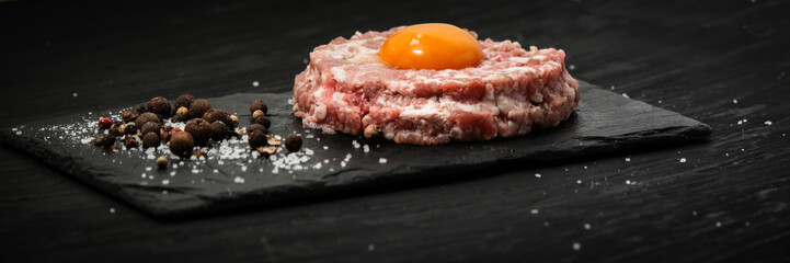 Raw ground meat with egg on a dark background, top view with copy space