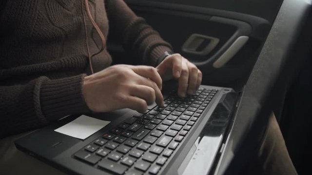 A man is working in a car typing text on a laptop