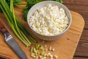 Homemade cottage cheese or curd in bowl and fresh green herb cutting board