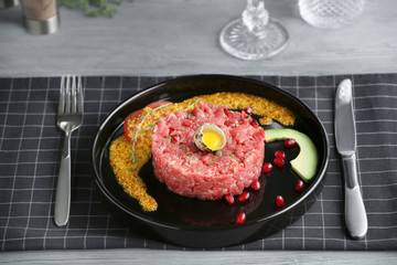 Delicious steak tartare with yolk in egg shell and pomegranate seeds on plate