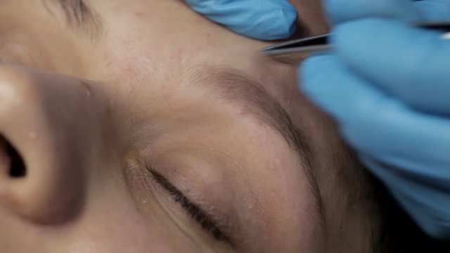 Cosmetologist makes eyebrow correction to client