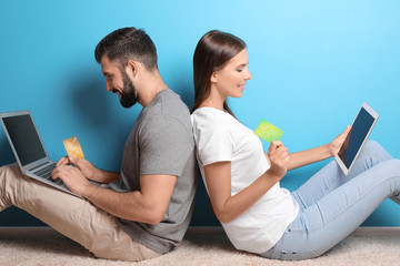 Young couple with laptop and tablet computer near color wall. Internet shopping concept