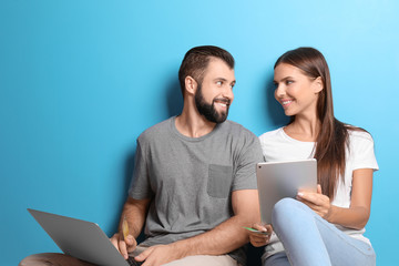 Young couple with laptop and tablet computer near color wall. Internet shopping concept