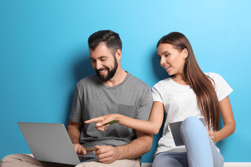 Young couple with laptop and tablet computer near color wall. Internet shopping concept