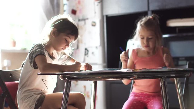 two sisters 6 and 7 years drawing together sitting at the table. children draw with crayons in the sun