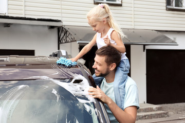 Man with little daughter washing car outdoors