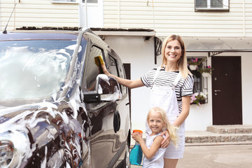 Woman with little daughter washing car outdoors