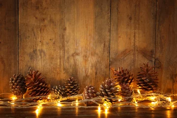 Deurstickers Holiday image with Christmas golden garland lights and pine cones over wooden background © tomertu