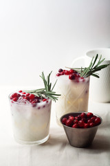 Perfect christmas cocktail: coconut margarita with cranberries and rosemary. Minimalistic concept. Linen cloth and white background. Vertical composition with copy space.