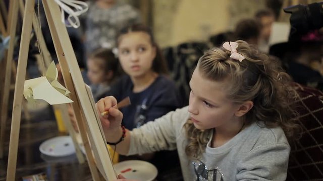 beautiful teenage girl sitting at the easel paints a picture in an art school. Professional art school for children