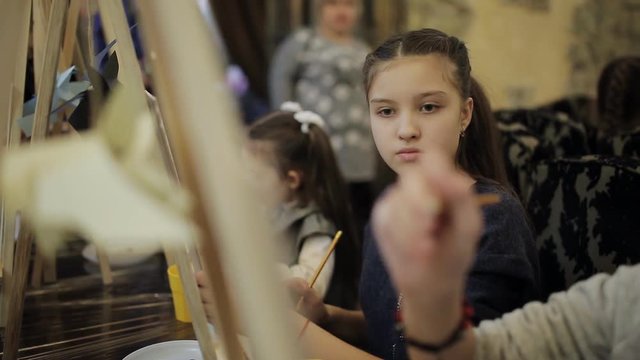 art school, a group of children with easels paint a painting with brushes and paints