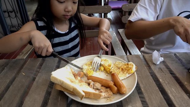 Asian Child Girl is eating breakfast using a steak knife, 5 year old
