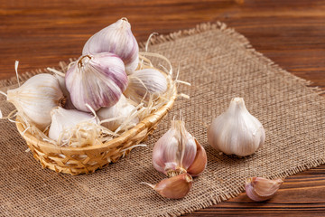 Garlic horizontal banner. Eco farming concept. Whole garlics and cloves in straw basket on piece of sacking on brown wooden texture background. Organic food.