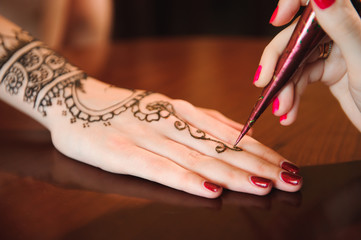 Master mehndi draws henna on a female hand.