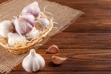 Garlic horizontal banner. Eco farming concept. Whole garlics and cloves in straw basket on piece of sacking on brown wooden texture background. Organic food.