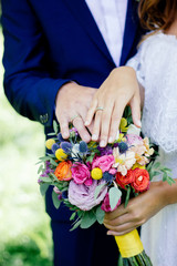 Bride and groom demonstrating rings on their hands against flower bouquet as background.