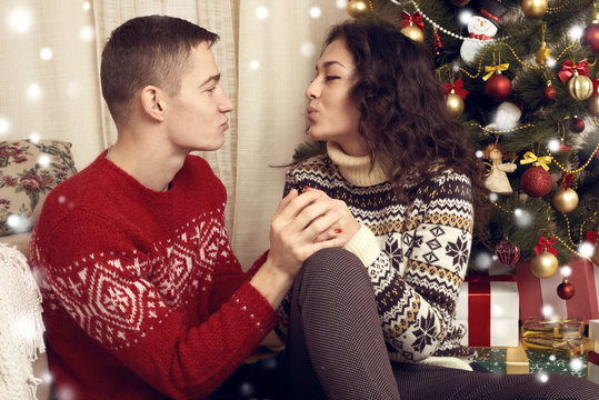 Happy couple kiss in christmas decoration at home. New year eve, ornated fir tree. Winter holiday and love concept.