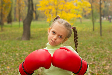 A little girl in huge boxing gloves makes an evil face.