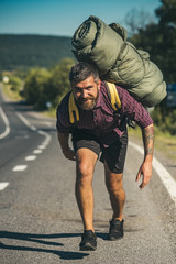 Fototapeta premium Man hiker happy bend under backpack on asphalt road