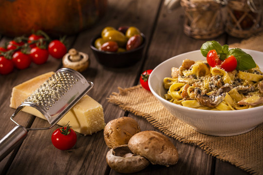 chicken and mushroom tagliatelle shot on wood boards at an angle with a copper pot loose mushrooms vine tomato parmesan block grater basil landscape