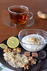 Breakfast table arrangement with jogurt, lemon, ground walnut and cup of tea..