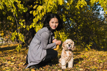 Attractive asian woman with dog in the park. Fallen leaves in the background.