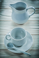 White ceramic cup saucer teaspoon creamer on wooden board
