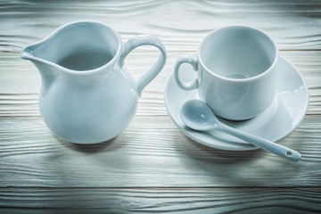 White ceramic cup saucer teaspoon milk jug on wooden board