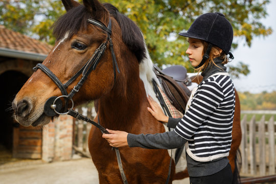  Preparing for training. Teenage girl with her horse in front of a stable