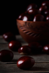 Fresh chestnuts in a bowl on an old wooden table. Group of chestnuts. Chestnuts - fruits horse chestnut - Aesculus hippocastanum. Dark background. Autumn background