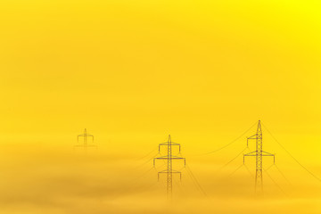 Row of electricity poles lines on field in morning fog during sunrise in the morning.